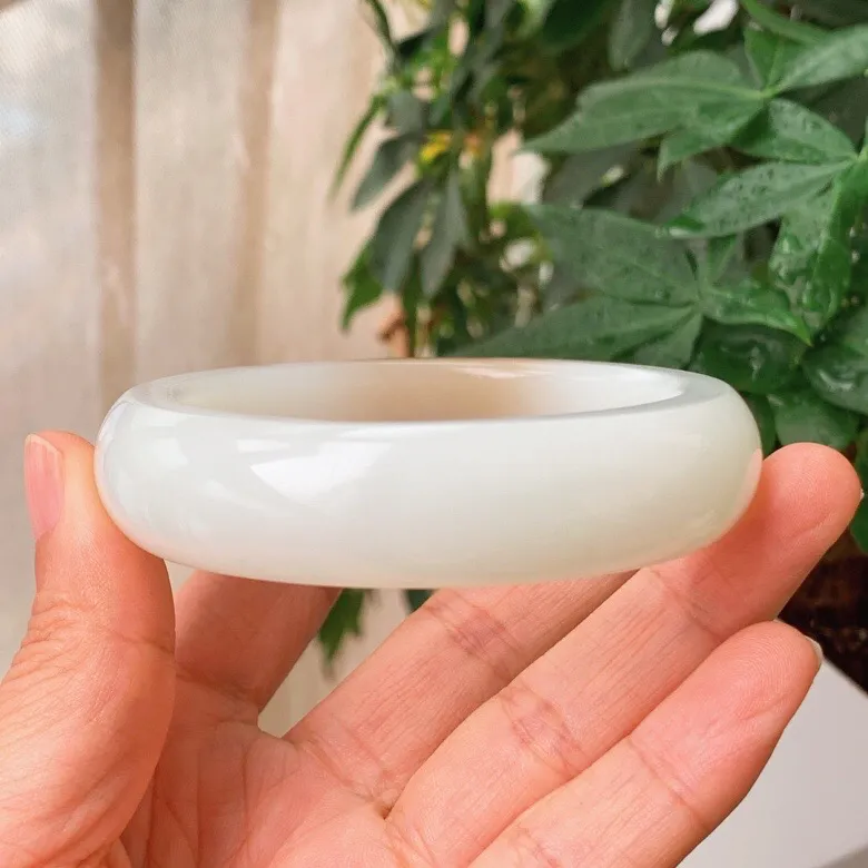 59圈口。新疆和田玉且末糖羊脂白玉手镯。且末糖一口糖手镯。圈口59条宽17厚10重89.9克。白度一级。玉质细腻油润。无裂无杂。手推出油。品相大气。 lt251013
