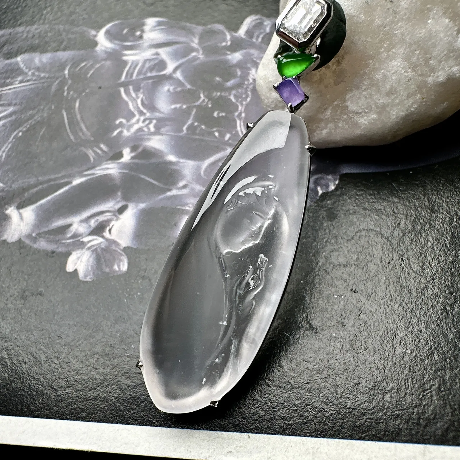 【玻璃种观音首吊坠】侧面像，料子通透闪亮，质地致密，种老起强胶感，玻璃光泽强烈。人物面部开脸生动，雕刻很精细，表情端庄祥和。料子纯净，18K金钻镶嵌，裸石尺寸33.3*13*2.8毫米