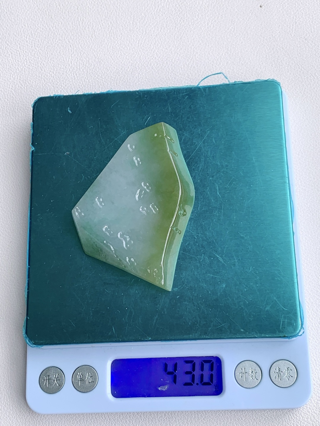 冰晴绿/冰飘花/牌子料/片料/板料/特色料，可做牌子、人物、山水、动物、花件……等推荐参考，61.5-44.9-7.4，43克，山衔浅黛凝清露，玉染轻烟蕴翠痕，这块冰润晴底带彩翡翠料子，底色温润通透如月光铺洒，边角晕染暖柔浅黄，一抹飘花翠色灵秀点缀其间，玉质细腻莹亮、水头充盈饱满，稍加匠心俏色精雕，便可化作山水意境牌、平安无事牌、悟道禅意挂件等雅致形制，浅暖翡色寓意温润纳福、和顺长久，点点翠花象征生机盎然、顺遂无忧自带清逸空灵的静谧氛围感，佩戴间衬得气质温润淡然，亦承载着山河安然、岁岁平顺、福运绵长的美好祈愿。