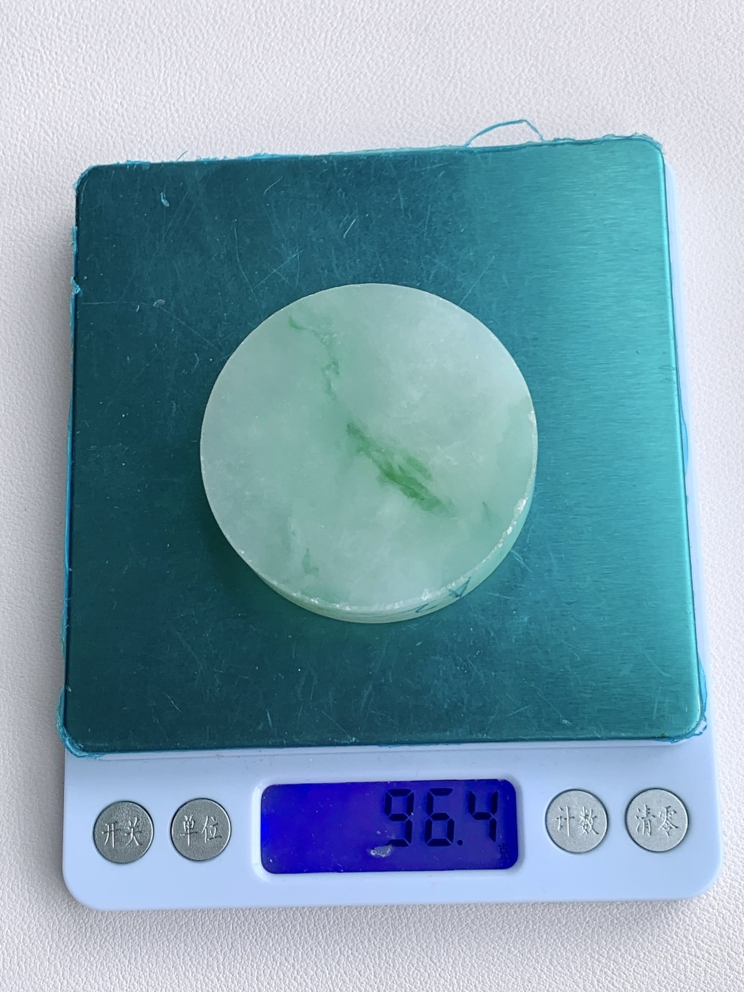 冰飘花 /牌子料/镯心料/特色料，可做牌子、人物、山水、动物、花件……等推荐参考，52.2-13.9，96.4克，材料优选，一圆清月凝冰魄，一缕飘翠画山川，这枚冰飘花翡翠圆牌胚料，质地温润莹净、水头灵透清亮，底色如月光铺洒般柔和淡雅，一抹浓绿飘花如远山含黛、似流水行舟，在素净玉面晕染出写意山水般的灵动意境，玉肉细腻胶润、品相规整圆满，稍加匠心雕琢，便可打磨成平安无事圆牌、怀古素圈、意境山水圆佩等雅致挂件，圆形象征圆满顺遂、团圆无忧，灵动飘花寓意前程舒展、生机绵延、福气生生不息气韵沉静温婉，佩戴可护佑岁岁平安、万事周全、福运圆圆满满、一生安稳无忧。