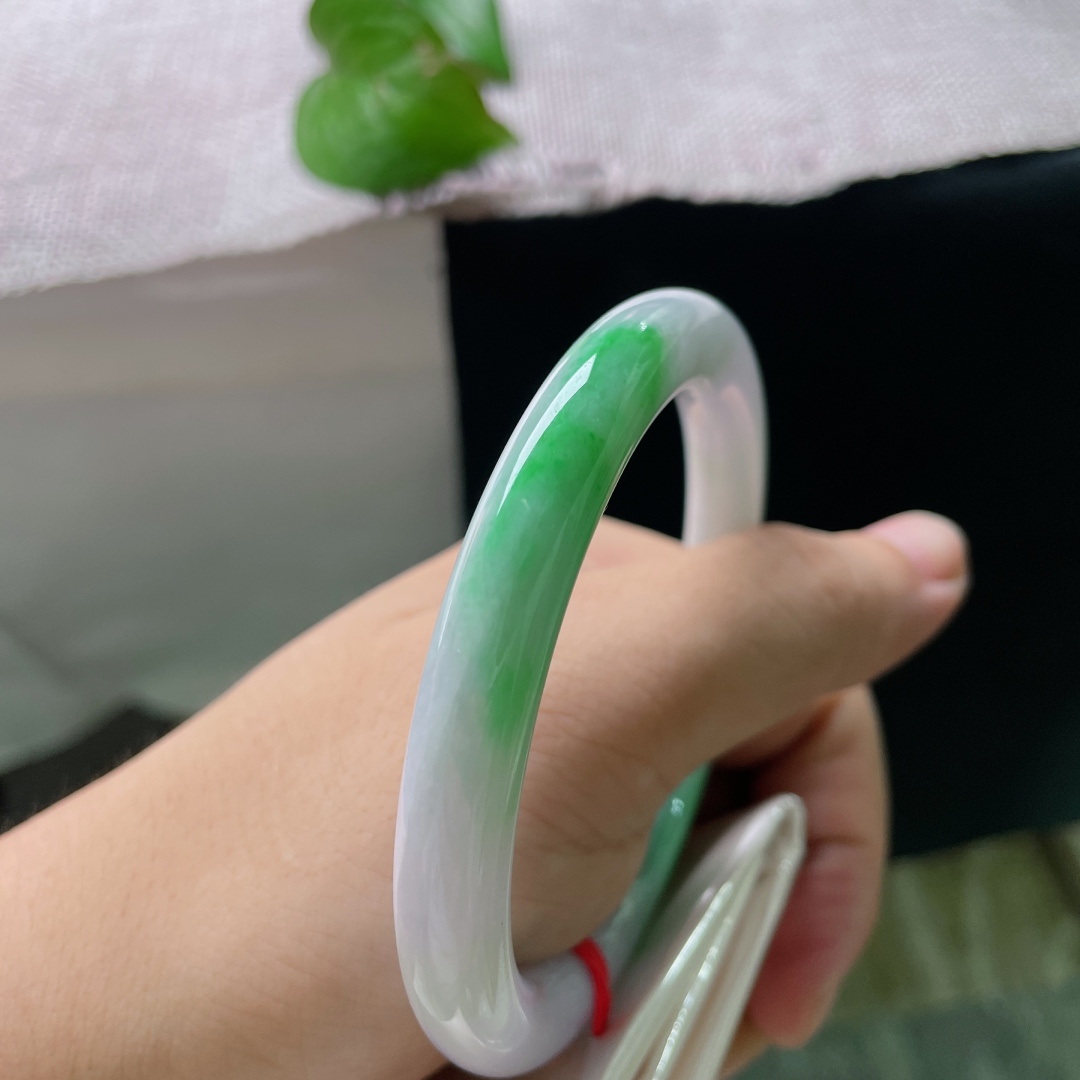 58.6/8.7，春彩圆条，横裂，基底是柔和温润的淡紫色，镯身两侧散落着几抹鲜亮的翠绿色飘色，色彩相融雅致协调，细腻有亮泽，佩戴起来温婉大方，自带清雅的古韵气质。ss53579a