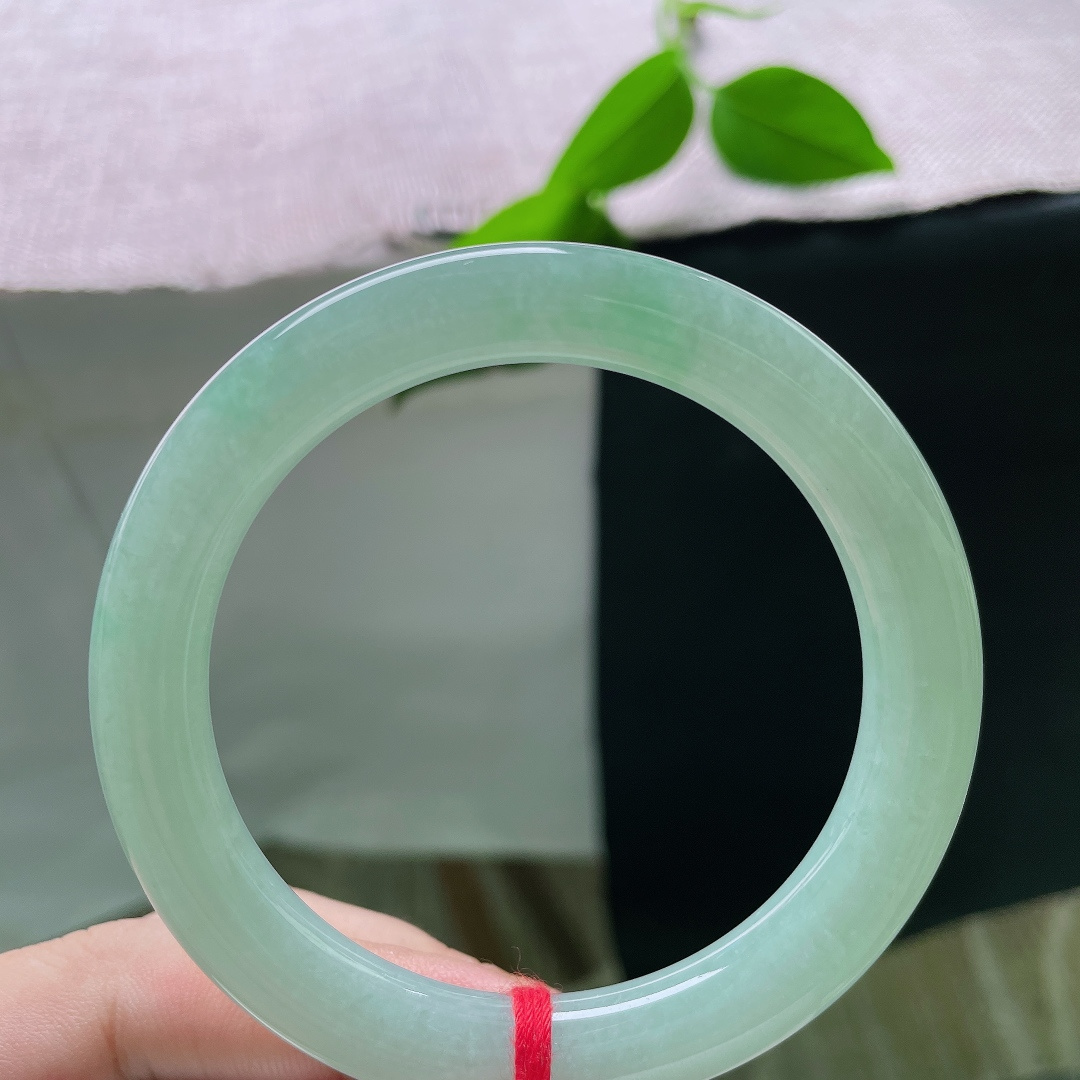 果绿圆条，有棉线，一镯凝露水，清翠润腕间。匀净浅绿温润通透，素面无华，以天然玉色勾勒简约中式温柔，沉静耐看，清雅动人。ss55981a