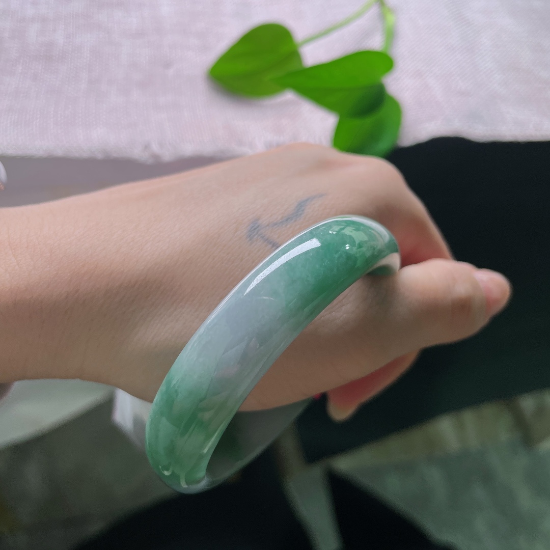 油青贵妃，一点皮纹，冰润飘绿正圈平安镯，半圈是清透的冰种底质，翠色如烟如云，自然飘散于镯身。ss58020a