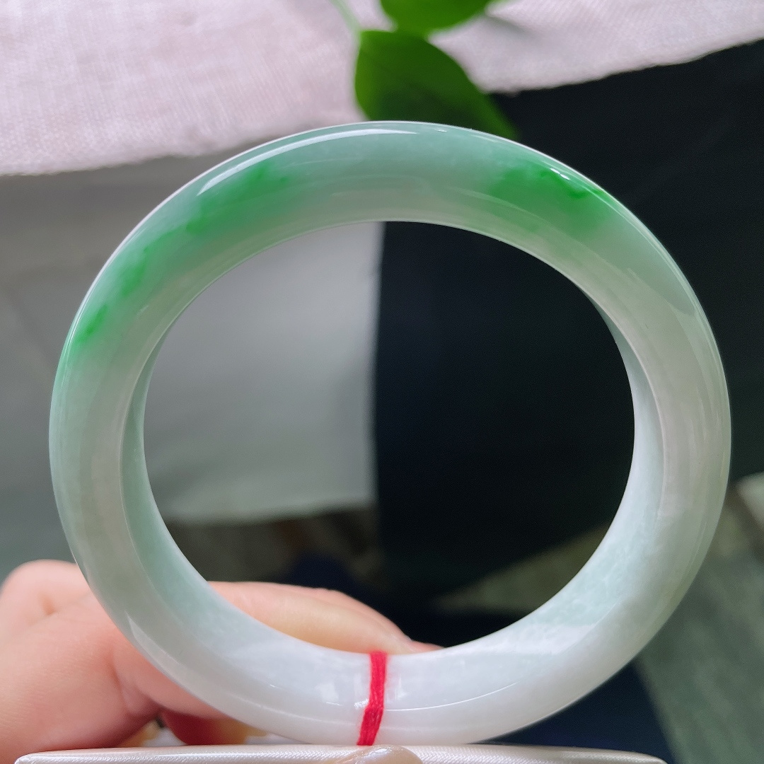 飘绿正圈，一点皮纹，几抹鲜活翠色错落晕染在镯身，绿意灵动鲜活，如同春日草木在玉底缓缓舒展。ss579