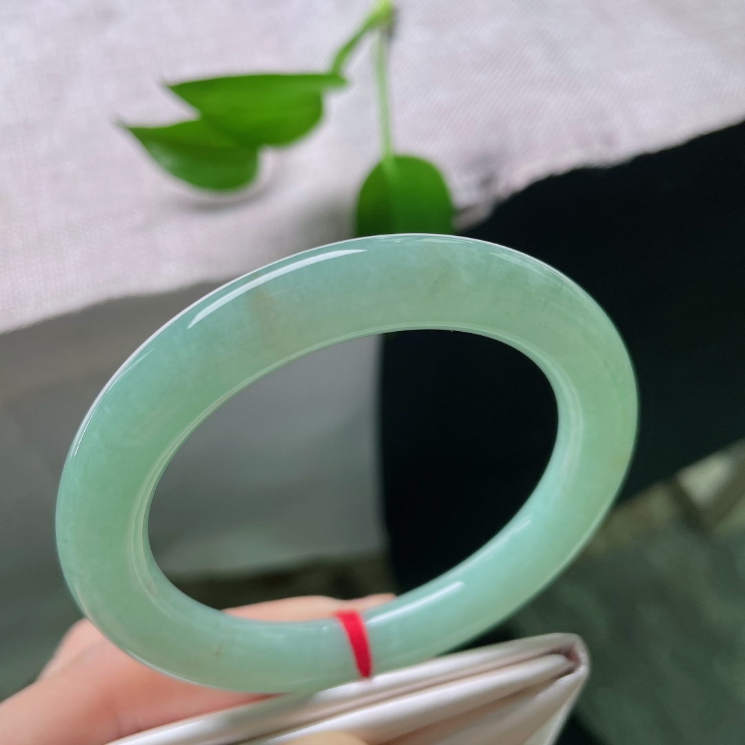 55.7/9.9，果绿圆条，棉线，镯型圆润饱满，玉质细腻，色泽恰似雨后新叶，清润鲜活，安静绽放在温润的玉镯之上。ss59644a