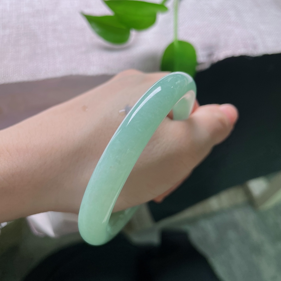 55.7/9.9，果绿圆条，棉线，镯型圆润饱满，玉质细腻，色泽恰似雨后新叶，清润鲜活，安静绽放在温润的玉镯之上。ss59644a